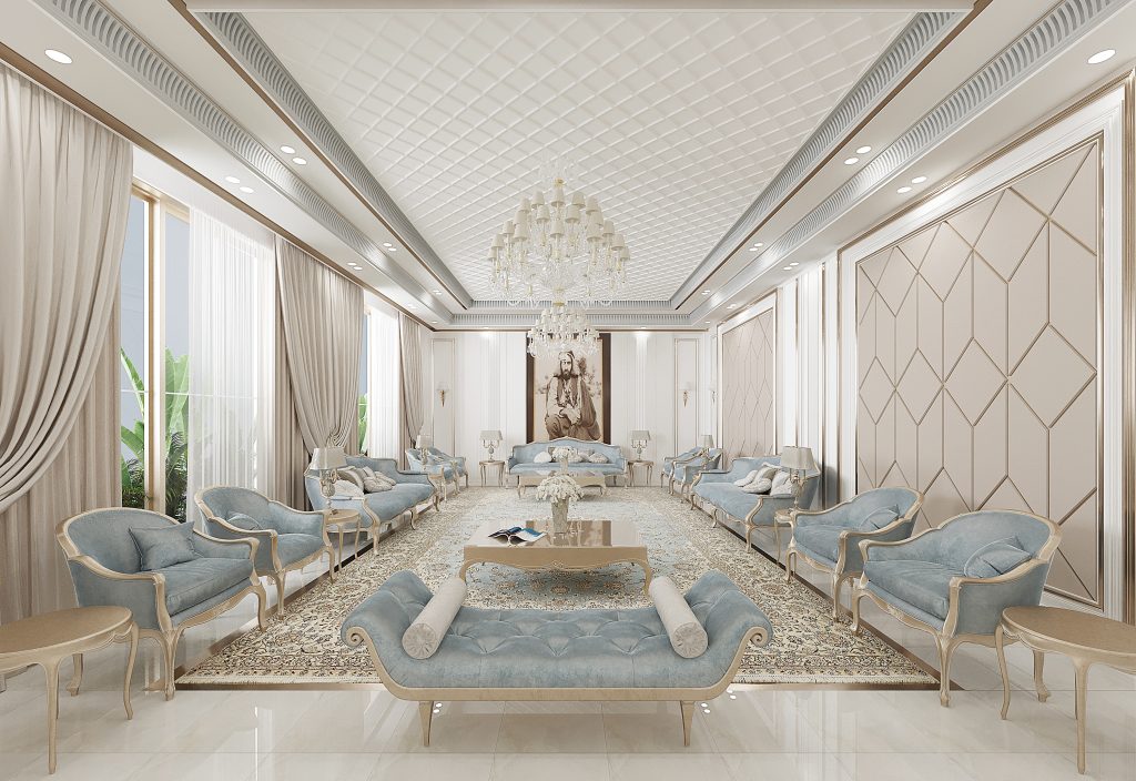 Luxurious majlis interior with an elegant and symmetrical layout featuring pastel blue tufted seating, cream and gold detailing, and a long ornate rug anchoring the space. A large crystal chandelier hangs from a quilted ceiling, while sheer curtains frame tall windows, and a regal portrait adds a focal point of SHEIKH ZAYED at the far end of the room